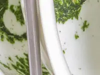 A lot of spinach food waste on a series of bowls in the upper rack of a dishwasher.
