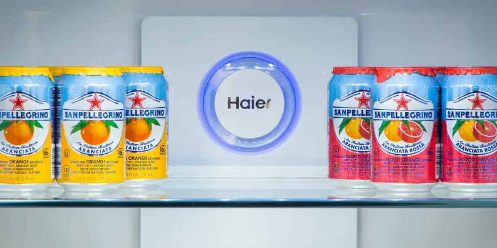 A fridge shelf is stocked with colorful cans of soda