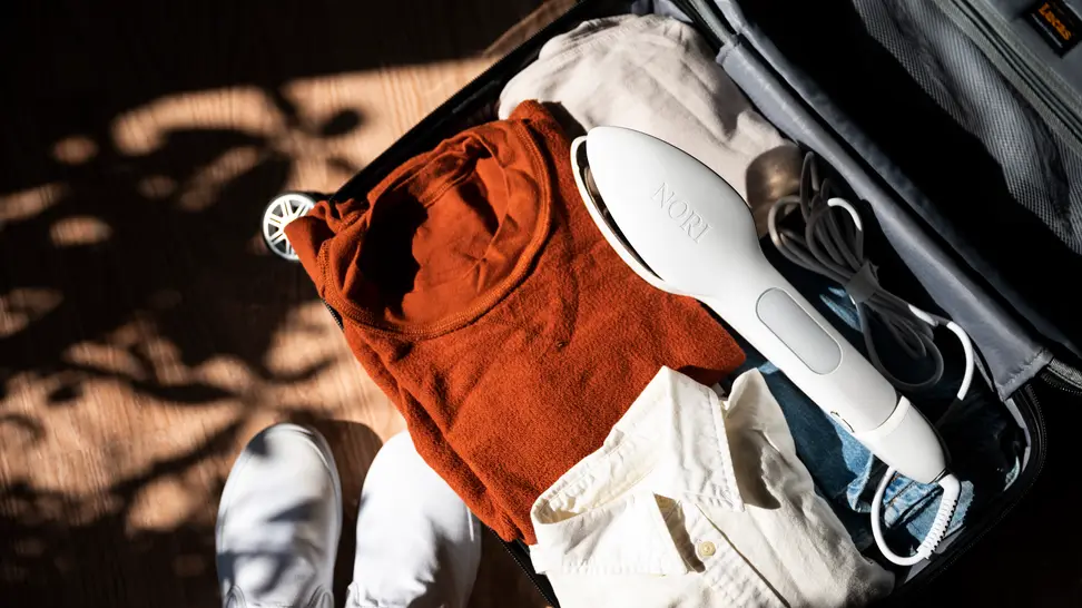 A travel iron sits in an open suitcase that's filled with clothes