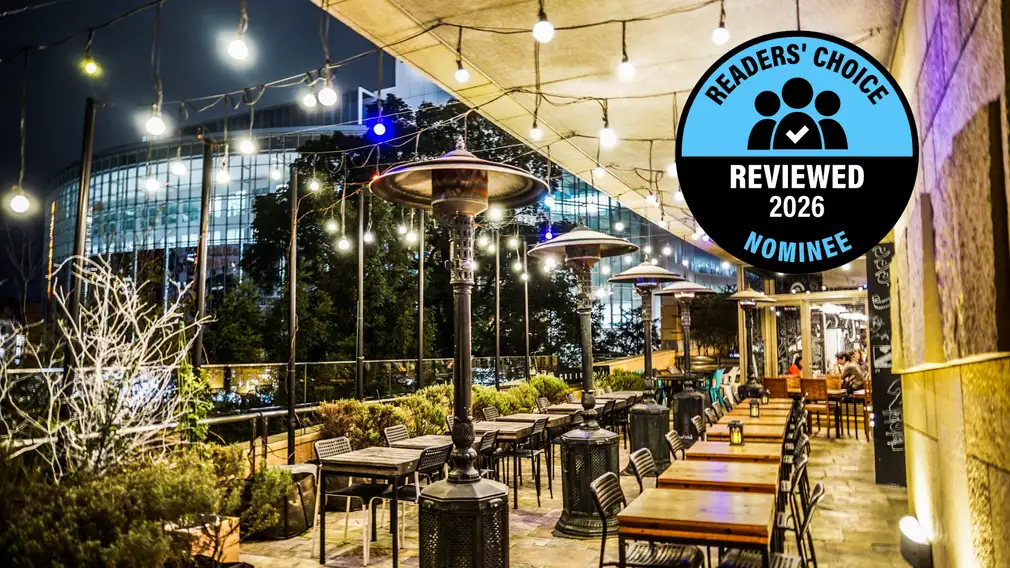 A string-lit outdoor patio dining area with tables, chairs, and patio heaters, with a "Readers' Choice Reviewed 2026 Nominee" badge.