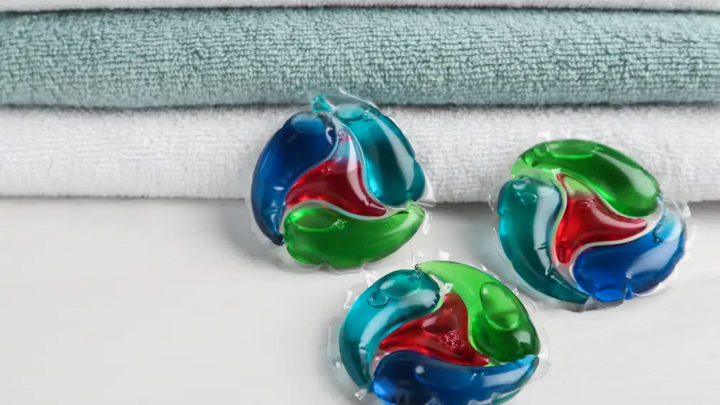 Three laundry pods placed next to folded towels