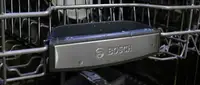 A close-up of the front of a Bosch dishwasher's top rack, which has the Bosch logo on it.
