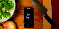 Bird's eye-view of a black smartphone screen on a countertop with a knife and salad plate.
