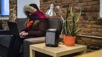 A woman sits on a couch in a cold room wrapped in a jacket.