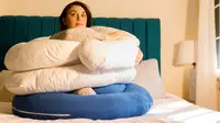 Writer Steph Garcia sits on a bed surrounding by pregnancy pillows.