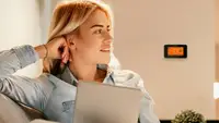 A woman sits down with a Sensi smart thermostat pictured on the wall behind her.