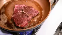 A bone-in steak cooks in a skillet filled with butter.