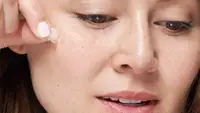 A woman taking a pimple patch off of her face.