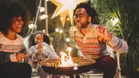 A family laughs around an outdoor fireplace