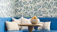 Blue wooden seating in the corner with white pillows and a blue floral decorative wallpaper from Rifle Paper Co.