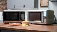 A pair of stainless-steel microwaves sit side by side on a wood-grain countertop.