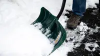 A close-up of a snow shovel digging into a snow bank. The person holding it is attempting to clear a walkway that's covered in a few inches of snow. .