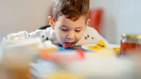 Cute little 2.5 year old boy licking some spilled milk of dining table