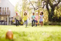 Five children run towards an Easter egg, baskets in hand and bunny ears on.