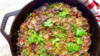 A close-up overhead photo of crispy potato kugel in a Lodge cast iron skillet, garnished with fresh parsley and dill.