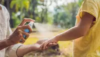 Person spraying mosquito repellent on child's arm while outdoors