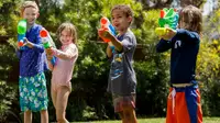 Four kids lined up outside shooting water guns and Nerf Super Soakers