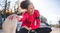 Woman stretching outside wearing headphones and workout clothes.