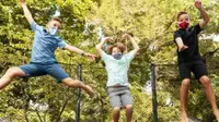 Three kids jump on a trampoline while wearing face masks.