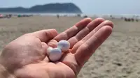 The all white Galaxy Buds 2 sit together in a hand raised with a sandy beach and mountains in the background.