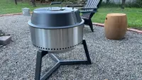 A portable charcoal grill sits on a pebble-covered yard.