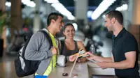 A man and a woman talking to a gym employee at the front desk.