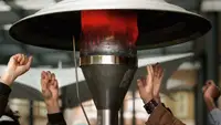 A small gathering of folks warm their hands around a glowing patio heater.