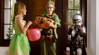 Three kids wearing Halloween costumes: Tinker Bell, Peter Pan, and the Mandalorian