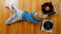 A child laying on his stomach on the floor listening to a record player.