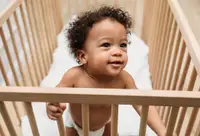 A small child stands up in a wooden crib.