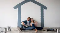 A couple sit inside a room underneath a painted house on a wall.
