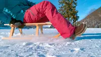 A model wearing snow pants glides across a frozen lake on a sled.