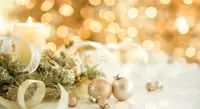Gold Christmas ornaments surround white burning candle and Christmas lights.