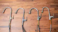 Four uninstalled kitchen faucets lay on their sides on a butcherblock counter