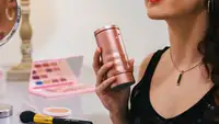 A person holding up a rose gold canister of perfume.