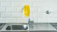 A pair of yellow rubber gloves lay on top of a faucet.