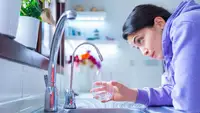 Person holding glass underneath faucet with water not running