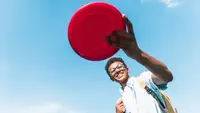 A child flings a red frisbee outside.