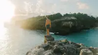 Man standing on a cliff in front of the ocean wearing blue swim trunks