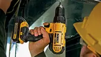 Photo of a person in a yellow helmet and safety glasses using a DeWalt drill.