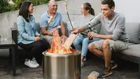 Group of people sitting around the Solo Stove Bonfire fire pit roasting marshmellows