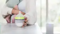 A parent reaches for a baby bottle filled with baby formula or breast milk while she holds her infant.