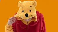 A person modeling their Winnie the Pooh costume onesie against a Halloween-orange backdrop.