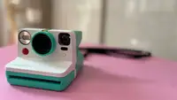 White, retro polaroid camera on pink tabletop.