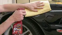 A guy cleaning his car with detailer from his car cleaning kit.