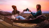 Two friends sitting on their camping hammock during a trip.