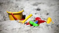 Colorful buckets, shovels, and other toys lie half-buried in beach sand.