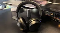 A pair of black headphones with a fabric-topped headband sit on a grey laptop on a black desk with gear behind it.