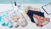 Six pairs of women's incontinence underwear from Speax, Knix, Always, Depend, and Wearever laying on a table with a measuring cup of water and a tray.