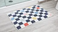A checkered bath mat sits on a gray floor by a standing shower